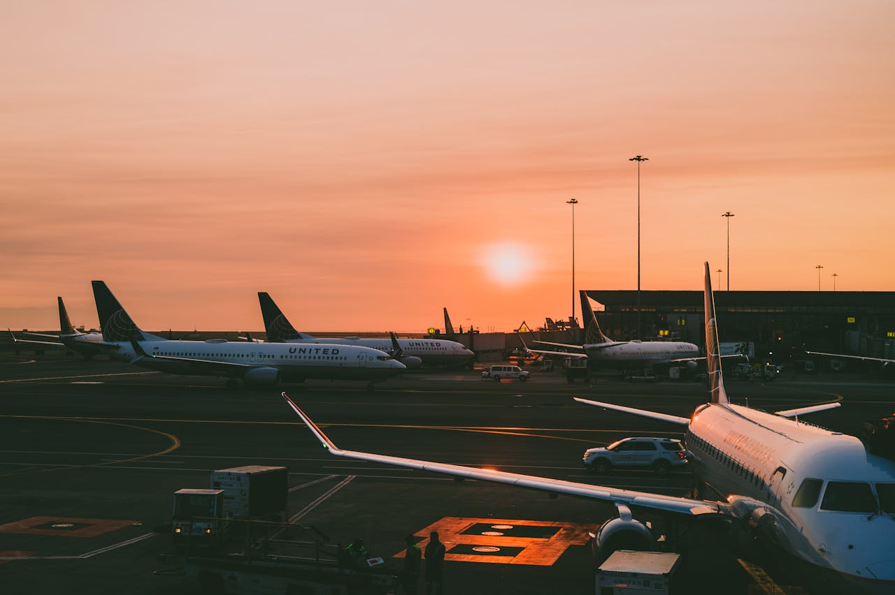 Services A serene view of parked airplanes at an airport with a beautiful sunset in the background.