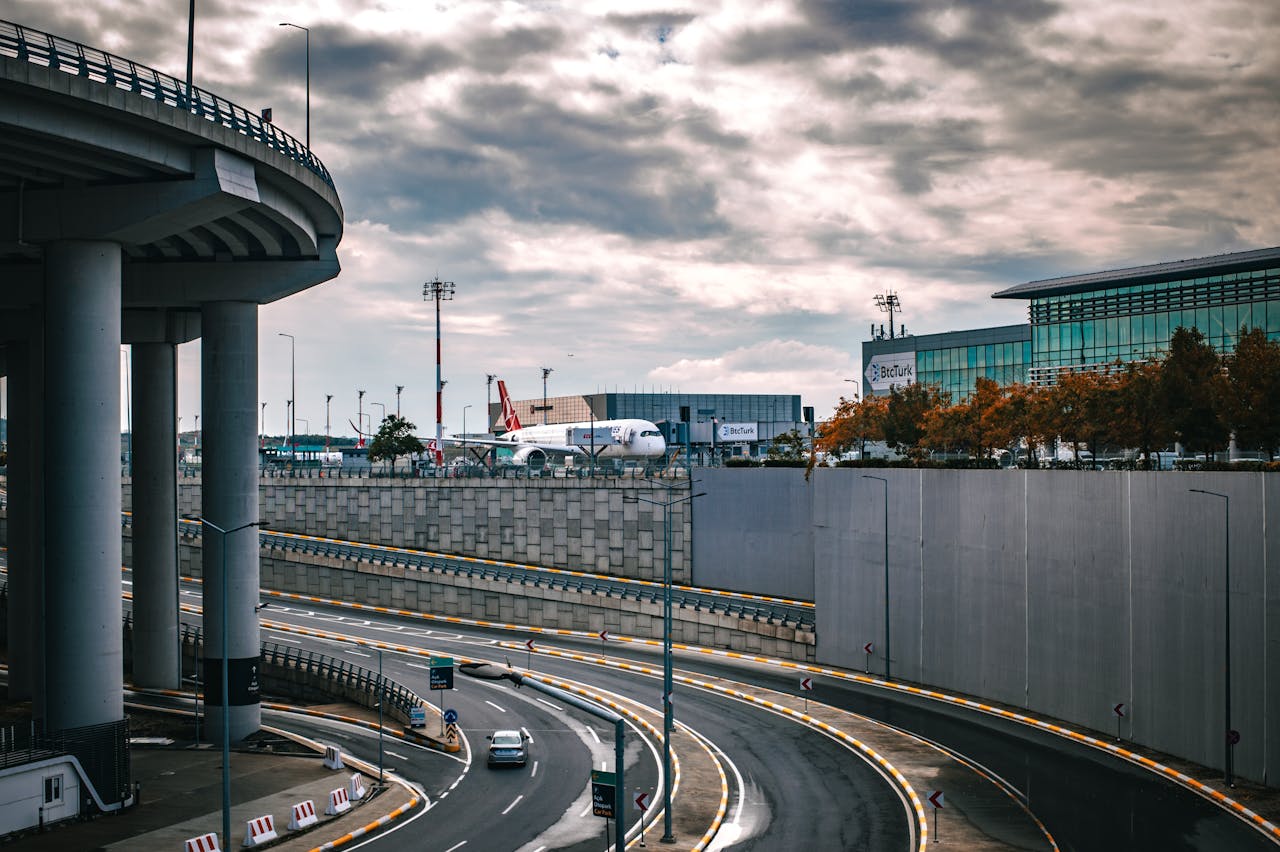 Services Urban scene featuring a busy airport terminal with an airplane and a highway under a cloudy sky.